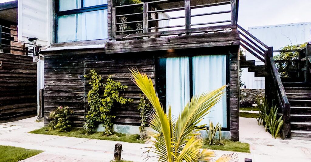 Contemporary two-story wooden house with lush greenery and palm plants.